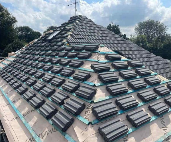 This is a photo of a new hip roof being installed. New felt, battens, and grey tiles have been installed, also a new velux window. Works carried out by DHG Roofing Shefford