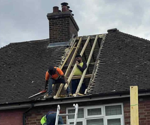 This is a photo of a roof repair being carried out. A section of the roof has been stripped and two roofers are replacing the rafters. Works being carried out by DHG Roofing Shefford